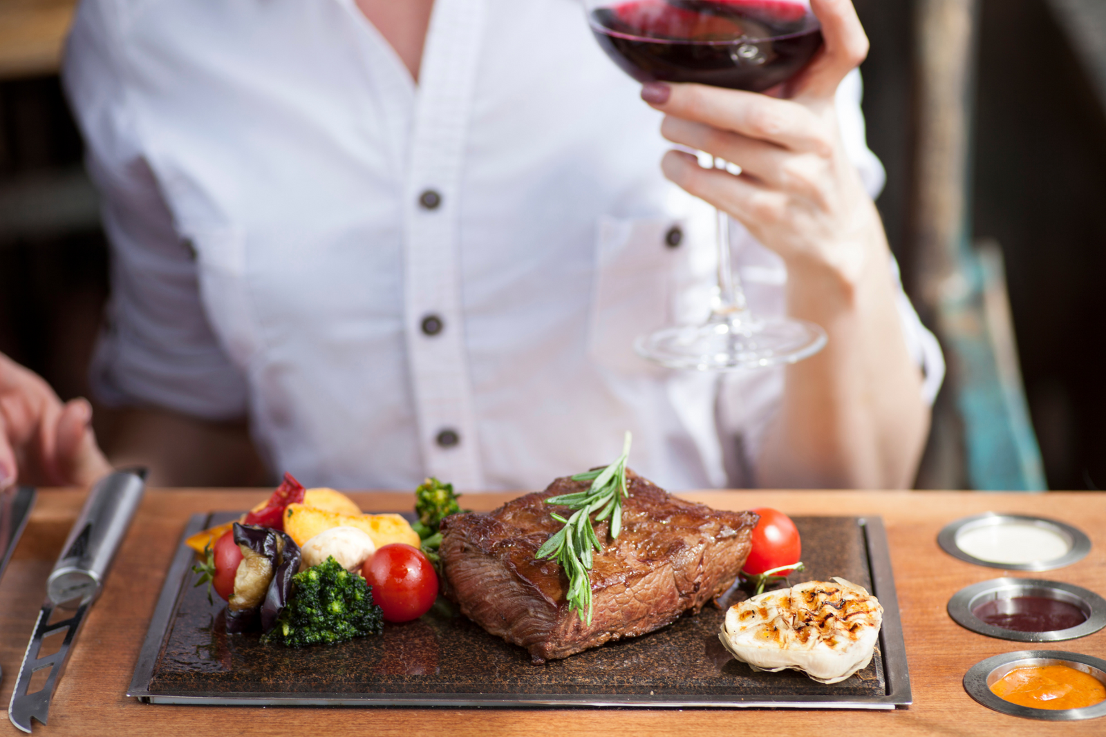 woman eating an ostrich steak dinner with red wine