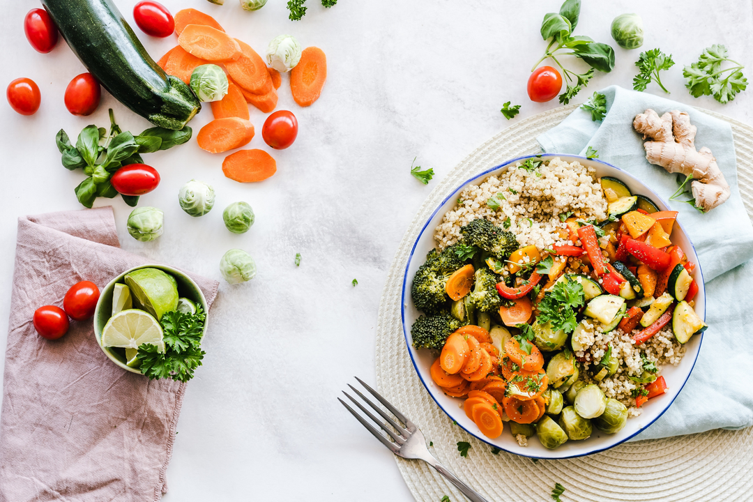 A table topped with scattered vegetables, as well as a plate of vegetables that are chopped and prepared to eat.