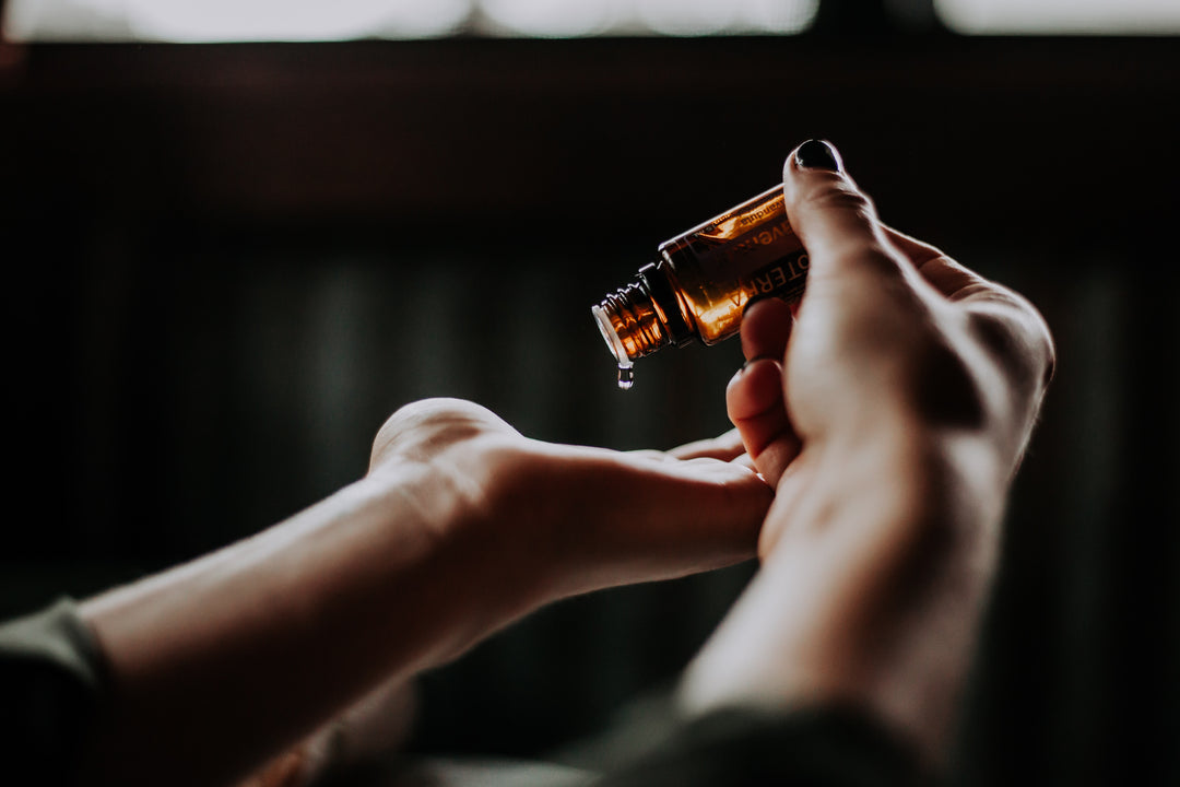 Close up of a person holding a small, dark brown bottle, putting a drop of clear oil on their palm. 