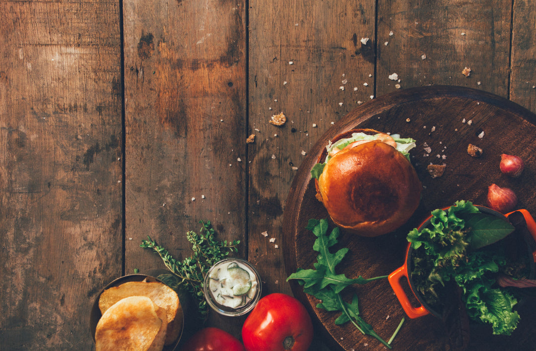 A burger, lettuce, chips, and tomatoes sit atop a wooden table.