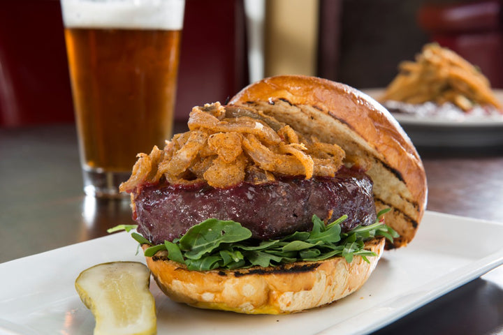 thick ground ostrich filet burger with arugula and crispy onions served with a pint of beer