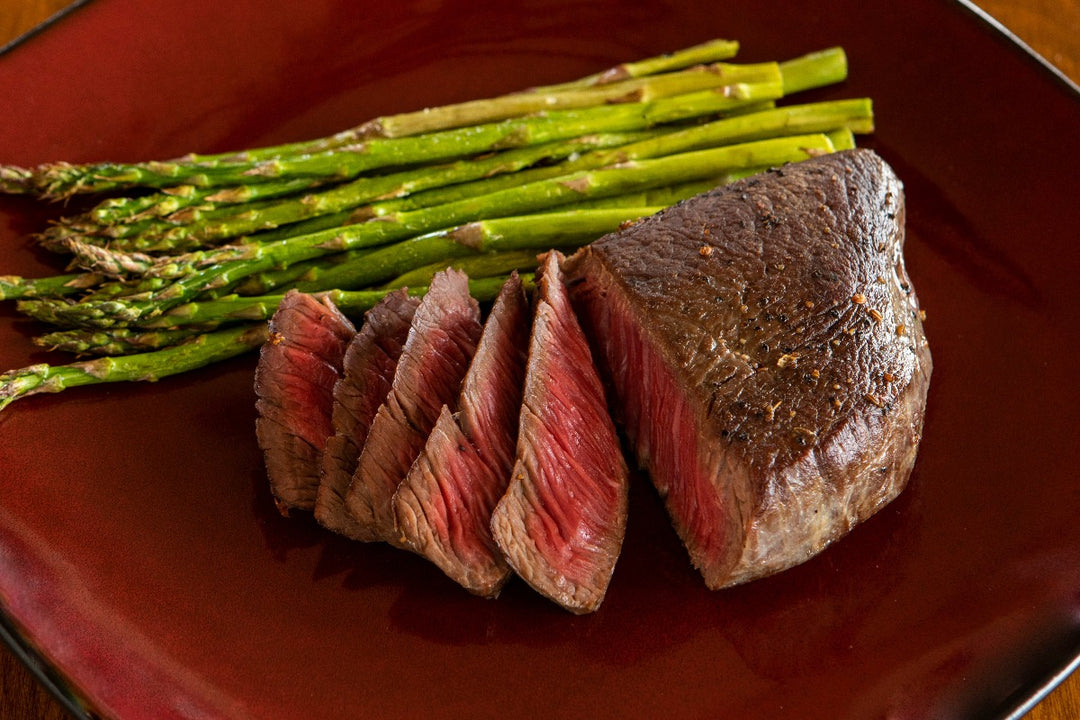 sliced cooked ostrich fan filet next to asparagus